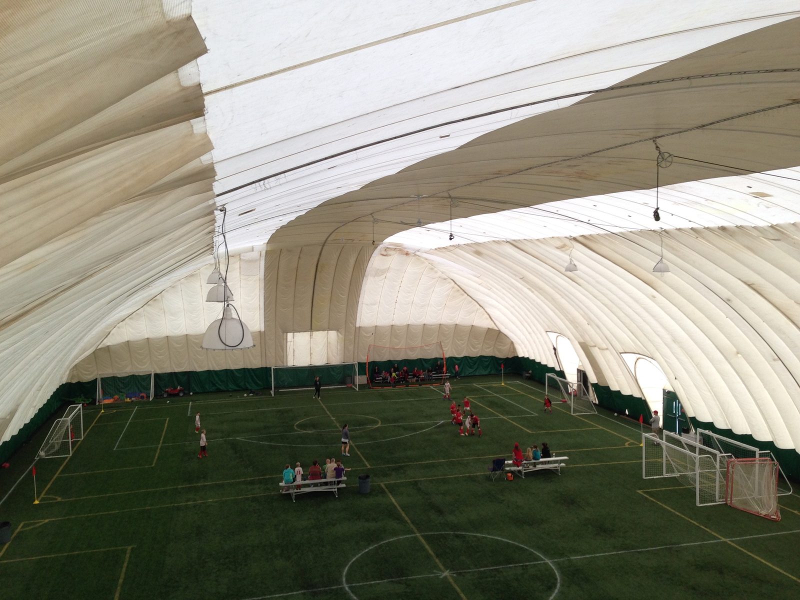 Inside an air-supported dome with artificial turf soccer fields, goals, benches, and youth players