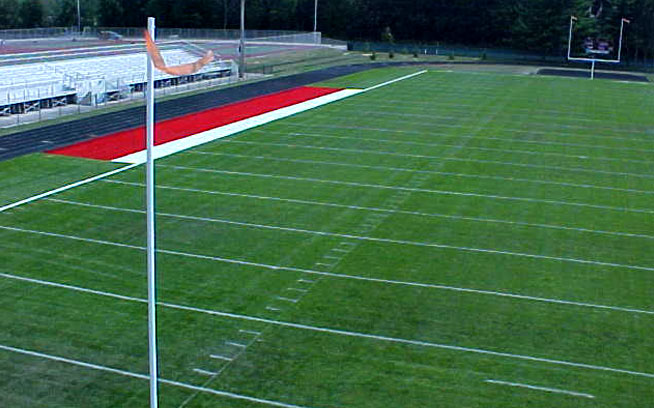 Artificial grass sideline area along a high school football field with bleachers