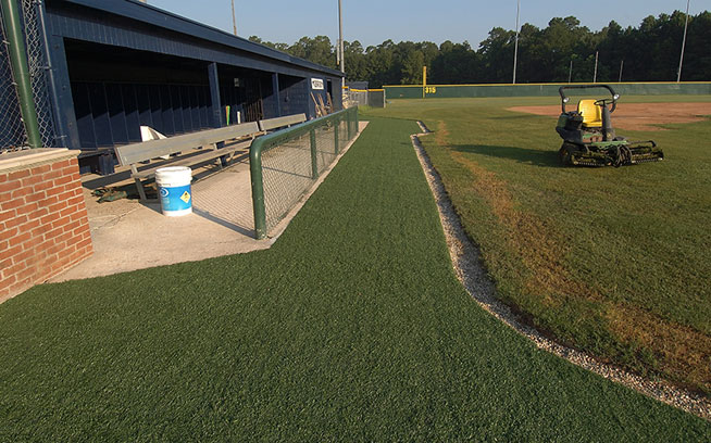 Artificial grass running along a baseball dugout and fence line